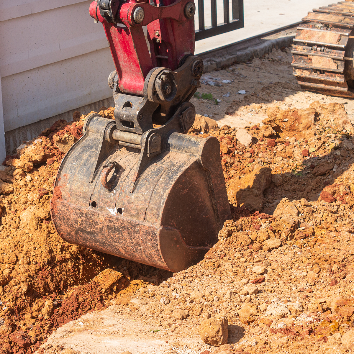excavator digging a trench along the foundation of a home